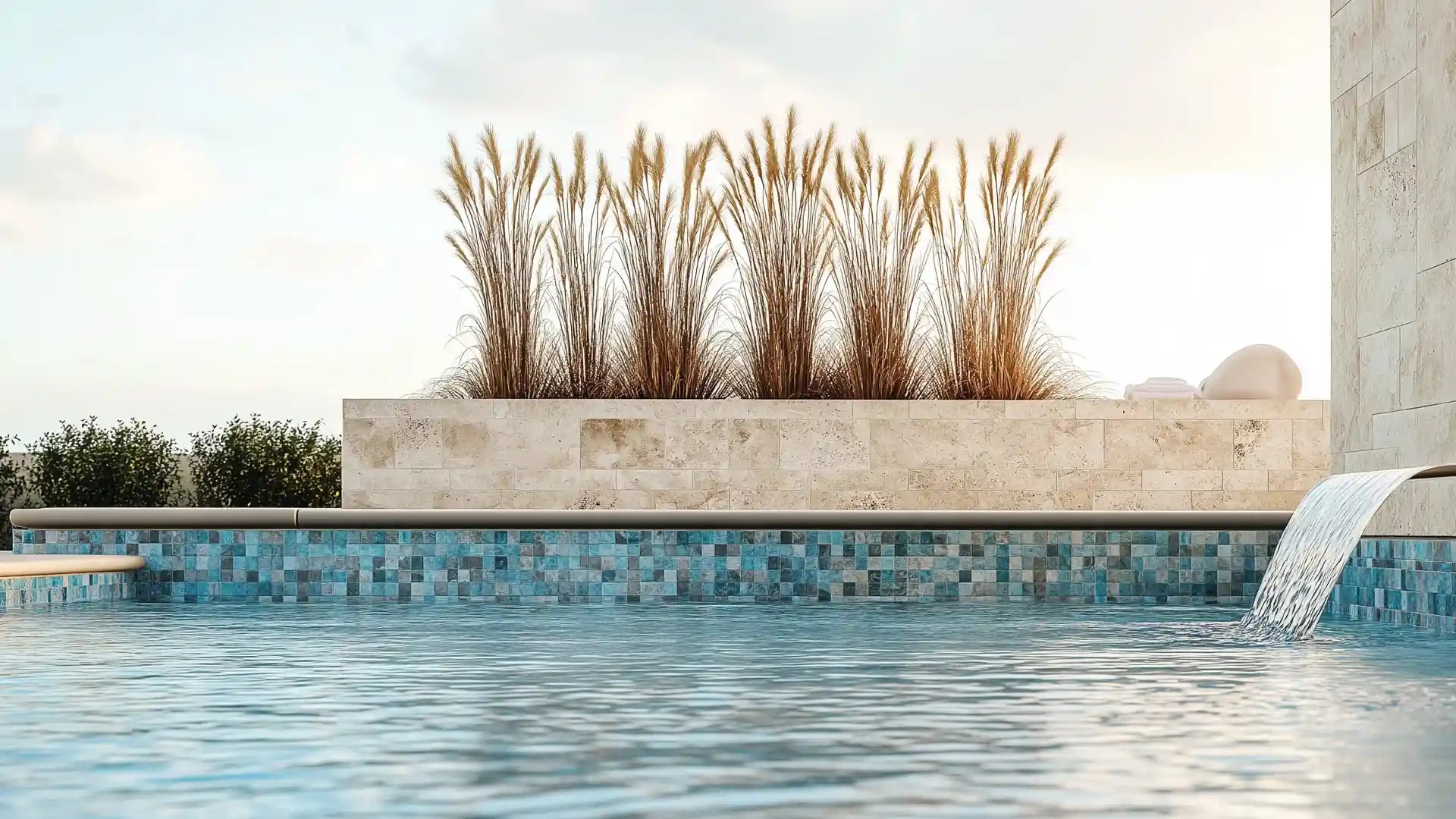 Blue mosaic glass pool tile wall with natural stone planter, waterfall spout, and ornamental grasses.